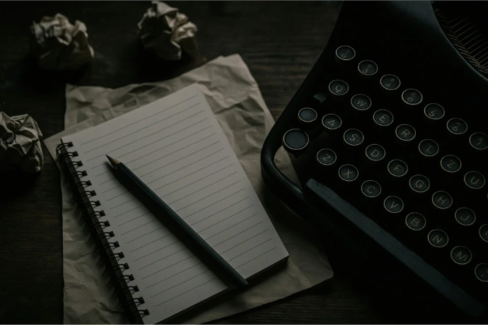 A typewriter, notepad, and crumpled paper are shown.
